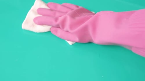 Gloved Hand Wiping a Teal Surface with Cloth