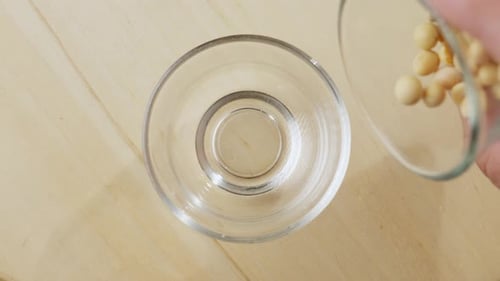 Overhead View Of Soybean Pods Slowly Pouring In Clear Glass Jar.