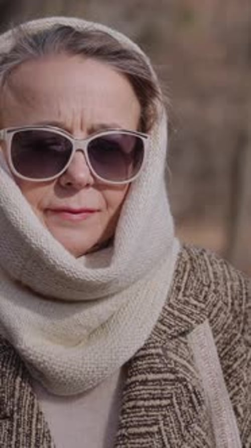 Vertical Old Lady Wearing Warm Scarf and Large Sunglasses Walks Across Park