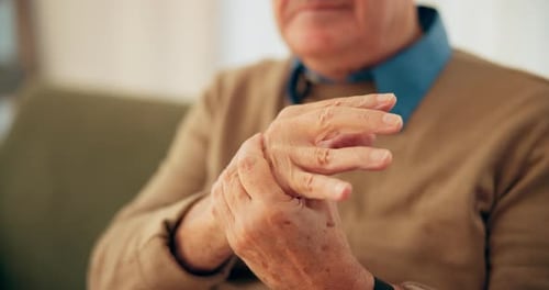 Nursing home, hand and senior person with arthritis or numbness of fingers in lounge, pain or sick