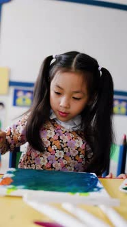 School art crafts, Asian child girl painting with brush on canvas paper at classroom. Vertical video