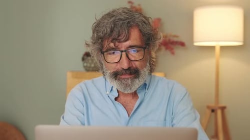 Close-up of an elderly man sitting in living-room with laptop looking at the camera with smile