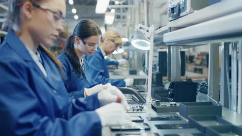 Une travailleuse d'une usine d'électronique en blouse de travail bleue et lunettes de protection assemble des smartphones