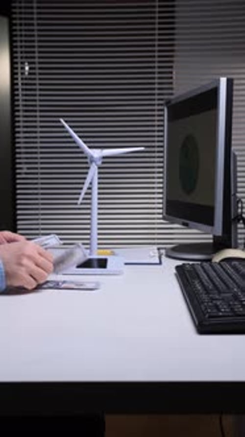 Vertical Video Person Counting Cash Next to a Wind Turbine Model and Computer Monitor Showing Data