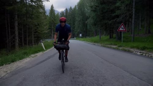 Man in sporty outfit cycles through the forest at a high speed on an early morning in the Italian mo