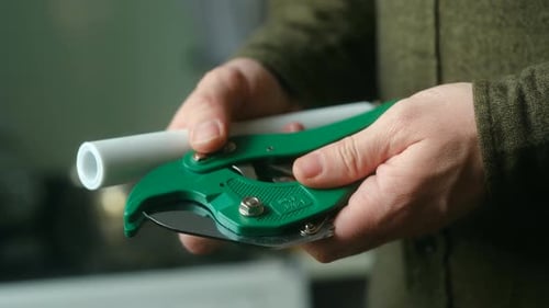 Hands Cutting White Pipe with Green Pipe Cutter