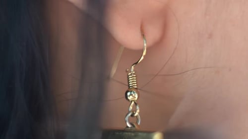 Close up view of a single earring hanging from the earlobe of a young woman, beauty, standards, luxu