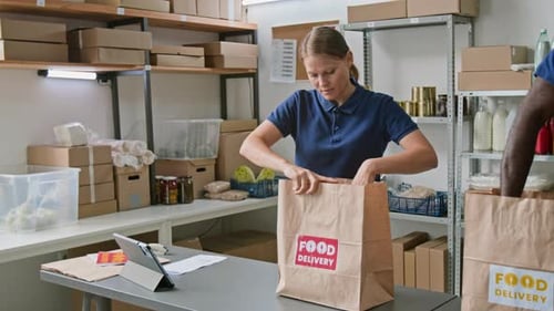 Female Dark Store Associate Stapling Order Invoice to Paper Bag with Groceries