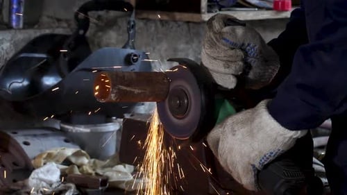 Trabajador cortando tubos de metal con amoladora angular creando chispas
