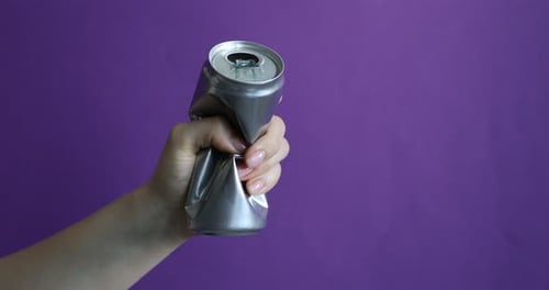 Mujer aplastando una lata de aluminio sobre fondo morado, primer plano. Espacio para texto