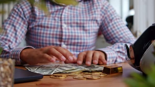 Person Counting US Currency with Gold and Laptop