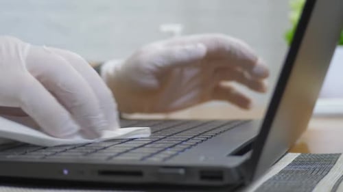 Man's Hands in Glove Spraying Antiseptic Cleaning Laptop Keyboard with Disinfectant Wet Wipe