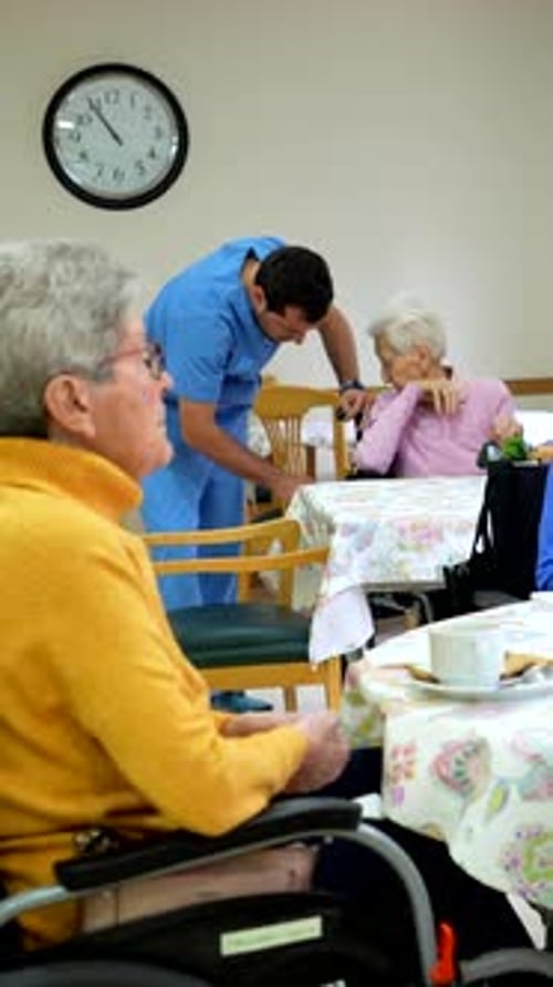 Elderly Woman Drawing in Nursing Home While Nurse Assists Another Patient