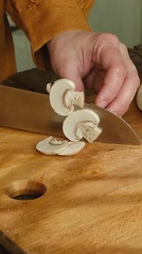Person Slicing Mushrooms on a Wooden Cutting Board
