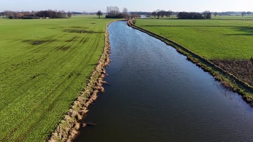 An aerial view captures a wide river or canal stretching through vibrant green pastures