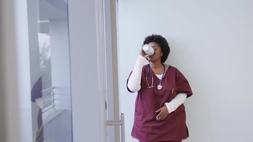 Tired african american female doctor drinking coffee in hospital, slow motion