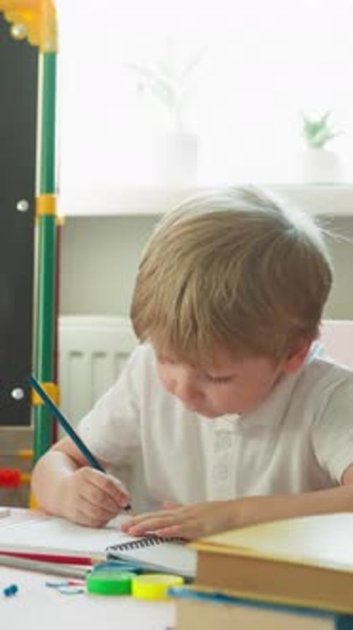 Blond Child Drawing with a Pencil at Desk