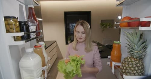 A Middleaged Woman Puts Food in the Refrigerator View From Inside the Refrigerator