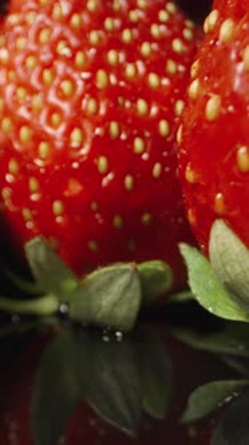 Juicy strawberries neatly arranged on a black mirrored table. Dolly slider extreme close-up.Vertical
