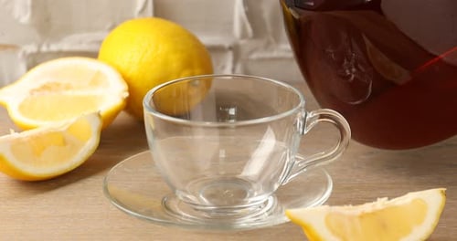 Pouring aromatic tea into glass cup at wooden table, closeup
