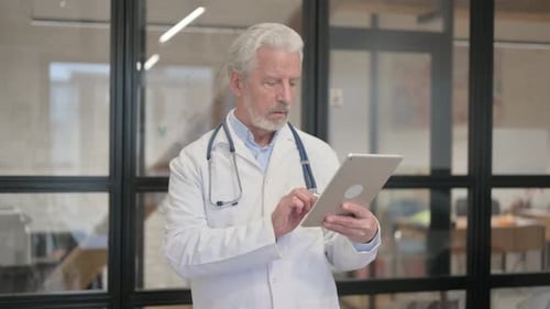 Senior Old Doctor Using Digital Tablet while Standing in Hospital
