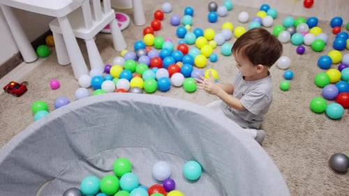 Little dark-haired boy sits near the dry pool. Lovely baby plays with sticker. Top view.