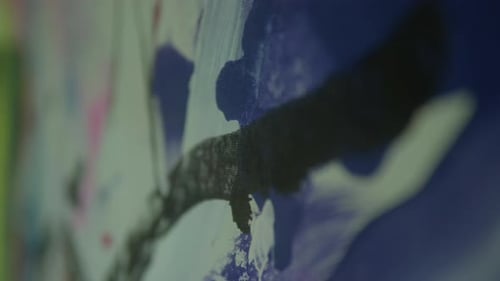 Close-up of an abstract painting with bold red, black, and pink brushstrokes on a white canvas