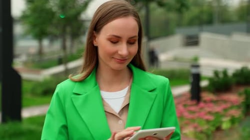 Happy Woman Checks the Contents of a Digital Tablet on the Street A Woman Walks Down the Street with