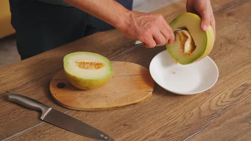 Man Prepares and Scoops Melon on Wood Table
