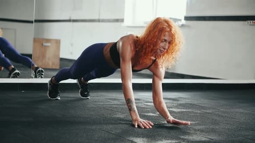 Sporty redhead girl with muscular body type doing push ups in gym