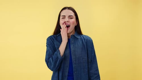 Femme épuisée couvrant la bouche avec la main tout en bâillant sur fond jaune