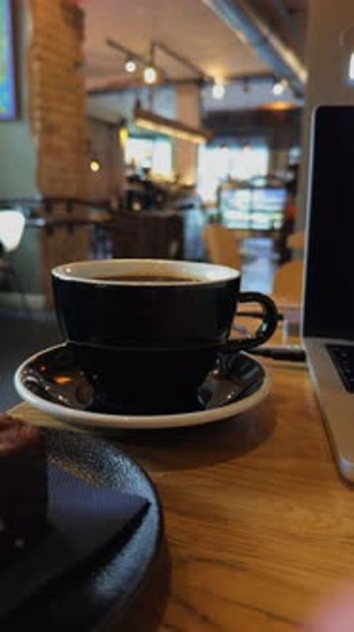 Enjoying Coffee and Working on a Laptop in a Cozy Cafe Setting with a Warm Ambiance and Delicious