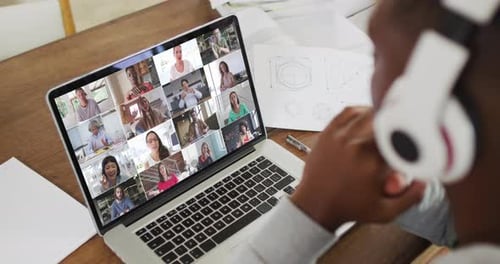 African american male college student holding notes and having a video conference on laptop at home