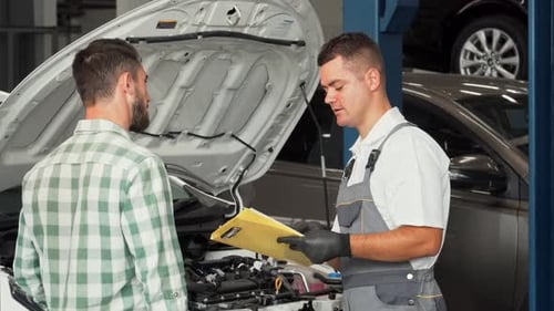 Freundlicher Automechaniker bespricht Reparaturen mit einem Kunden in einem Kfz-Servicecenter