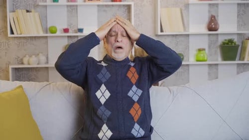 Mature Man Massaging Temples on Couch Indoors