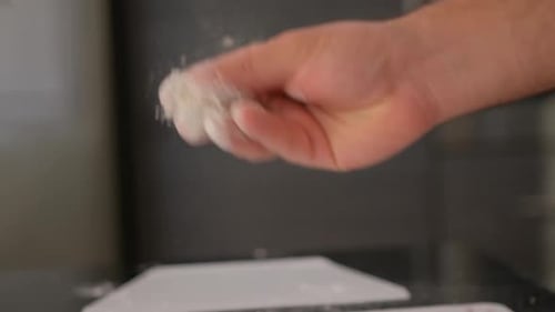 Nahaufnahme der Hand eines Bäckers, der in Zeitlupe Mehl bestreut.