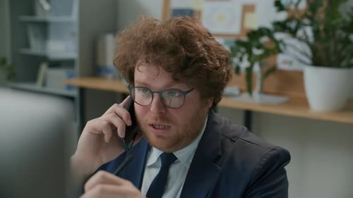 Businessman Talking on Phone and Taking Notes at Office Workplace