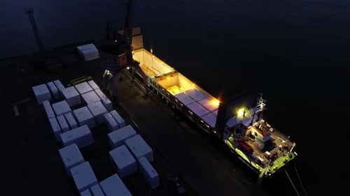 Crane loading shipping containers on a ferry at night - tilt down aerial view