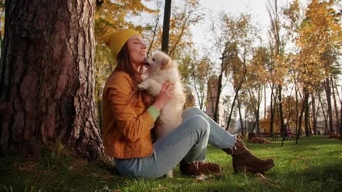 Happy Girl Hugging Pomeranian Spitz While Sitting By the Tree in the Forest