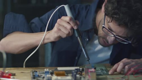 Student is studying electronics and soldering a circuit board in a garage.