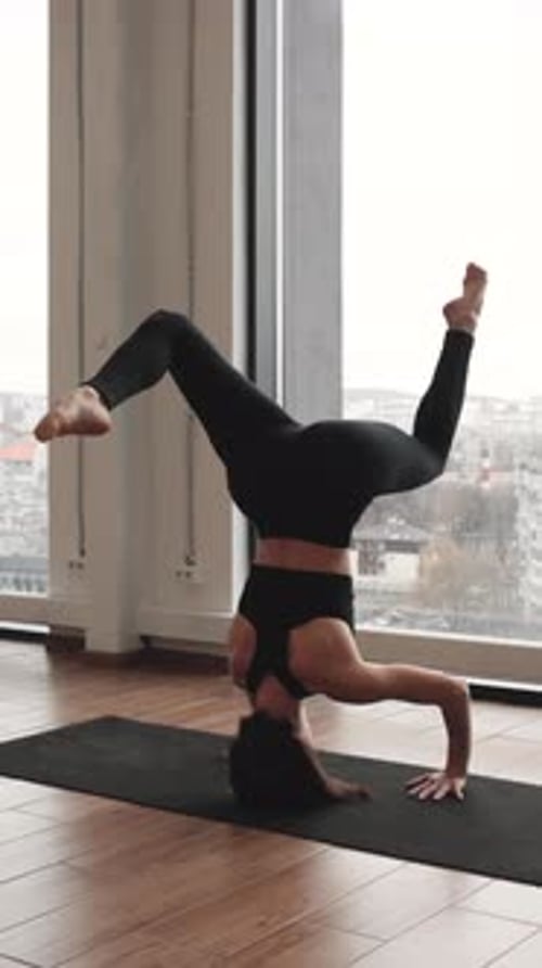 Woman Balances in Headstand Yoga Pose on Mat