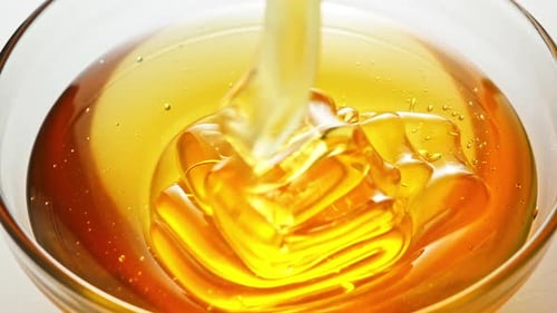 Honey pours into a transparent bowl on white background.