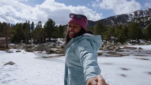 Smiling Tourist Holding Hand and Leading Partner Across Snowy Mountain Lake