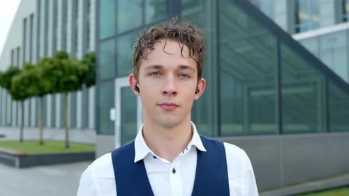 Junger männlicher Finanzanalyst trägt Ohrhörer mit selbstbewusstem Gesichtsausdruck im Freien im Front-Office