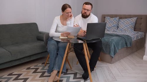 Couple Sitting at Table Discussing Documents With Laptop