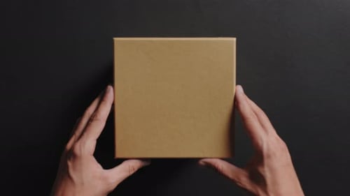 Hands Opening Brown Cardboard Box on Black Surface