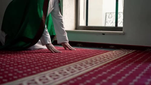 Ein muslimischer Gläubiger betet in der Dämmerung an einem Fenster in einer Moschee, kniet nieder und legt seinen Stirnteppich ab.