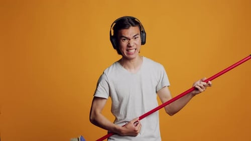Cara asiático despreocupado tocando guitarra com vassoura