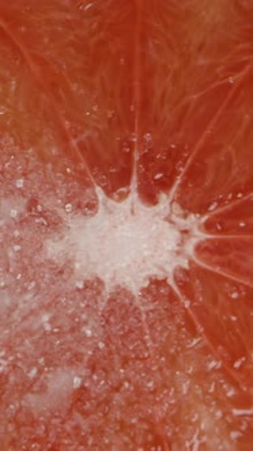 Vertical video. Top view of sugar being poured onto a half of a grapefruit. In slow motion. Dolly.