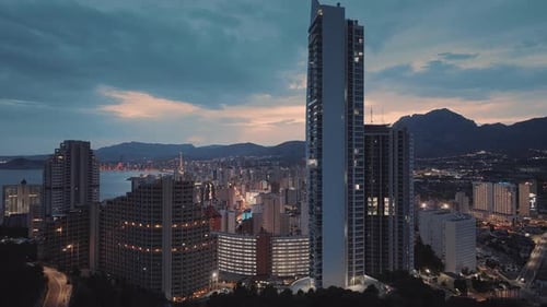 Bright seafront city with modern architecture in the evening. Pink sunset and mountains.